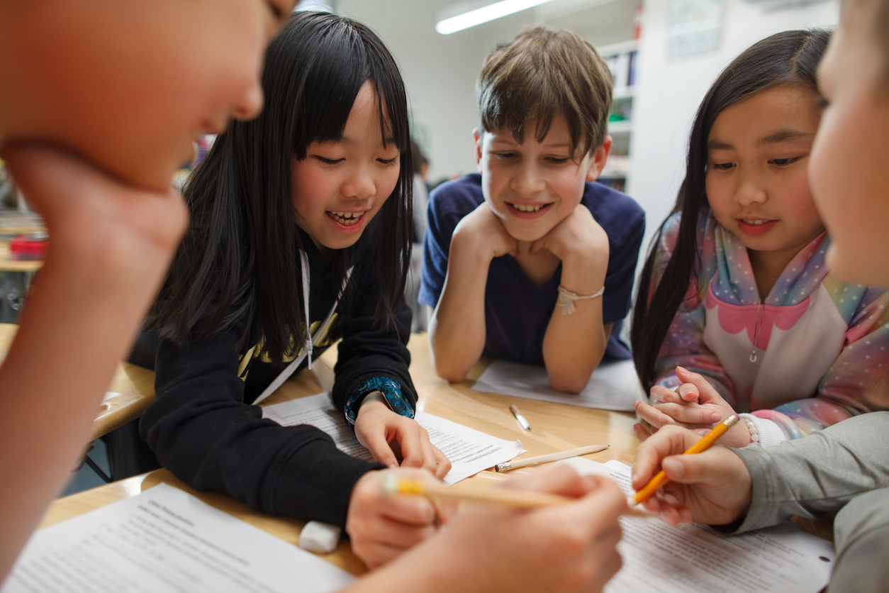 A group of students in a classroom around a desk doing work together