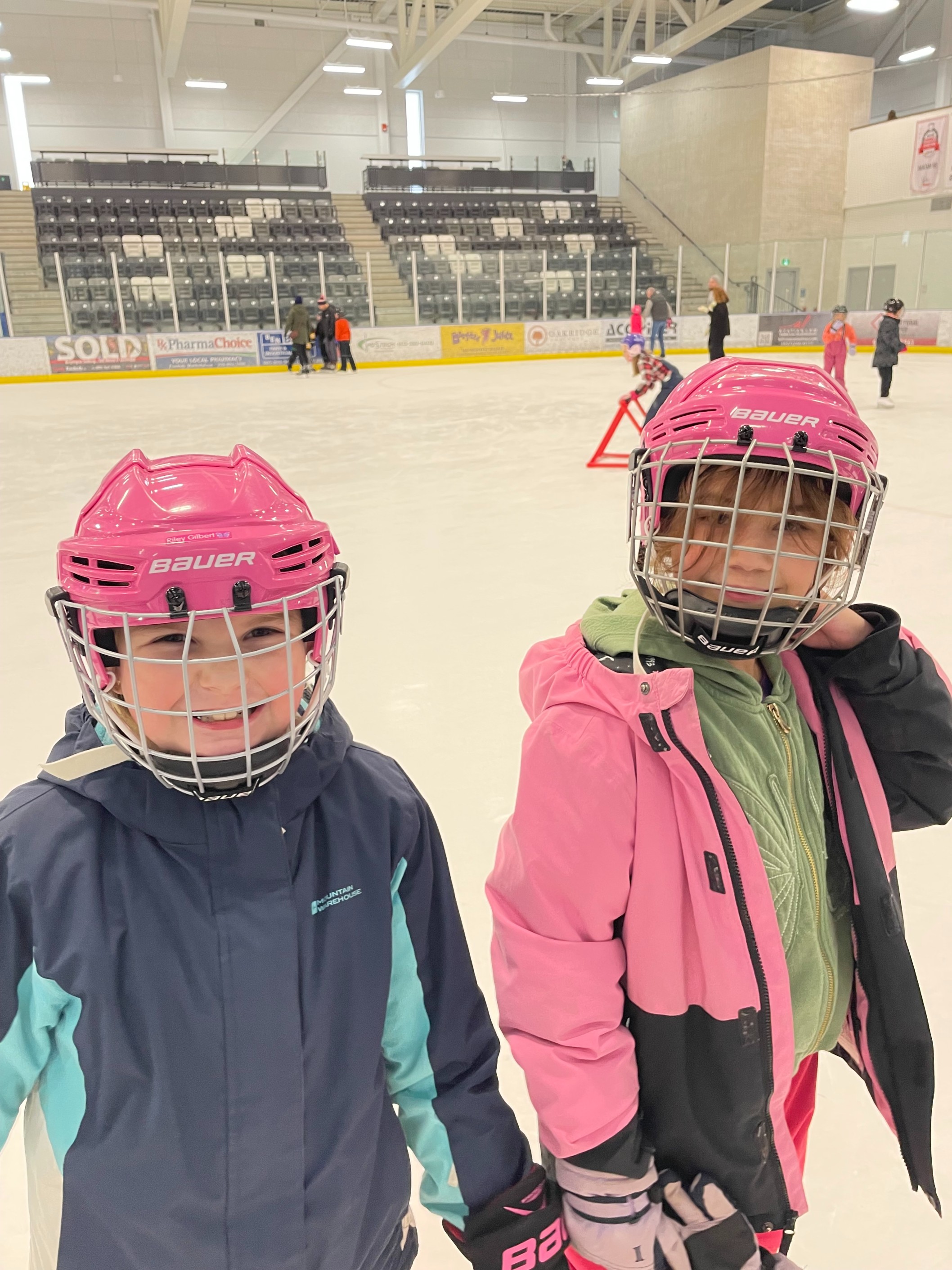 Deux élèves, portant des casques roses et des manteaux d’hiver, de l’École élémentaire Nouvel Horizon patinent ensemble sur une patinoire.